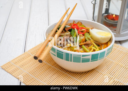 Il malese Mee Rebus nella ciotola con bacchette sul tavolo bianco questo piatto è fatta di tagliatelle ,,vegetale uova con un aroma di . Foto Stock