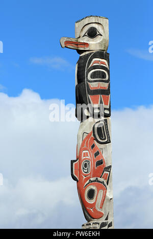 Native American bird e salmone motif totem pole con sfondo rosso, Foto Stock