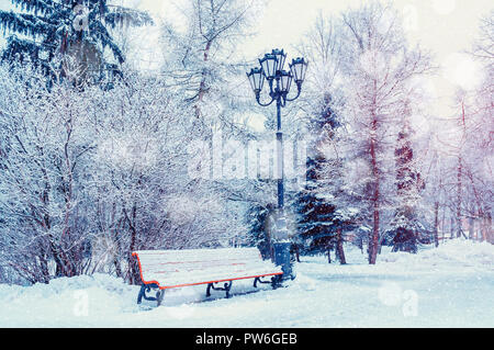 Paesaggio invernale con la caduta di fiocchi di neve- panchina coperta di neve tra gelido inverno alberi nel parco Foto Stock