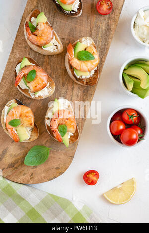 Bruschetta snack italiani panini con gamberetti, avocado e formaggio decorato con foglie di basilico. Foto Stock