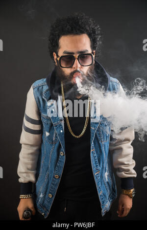 Uomo Vaping tenendo un mod. Una nuvola di vapore. Sfondo nero. Vaping una sigaretta elettronica con un sacco di fumo. Concetto Vape Foto Stock