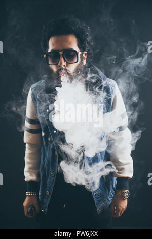 Uomo Vaping tenendo un mod. Una nuvola di vapore. Sfondo nero. Vaping una sigaretta elettronica con un sacco di fumo. Concetto Vape Foto Stock