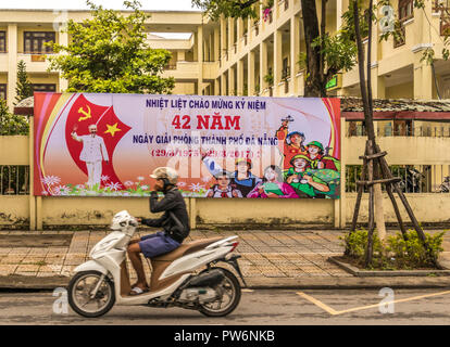 Motociclista in passato una delle molte comunità di Governo segni sulle strade di Da Nang Vietnam Foto Stock