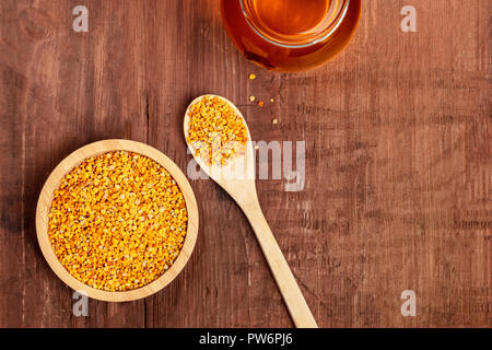 Un sano cibo biologico. Polline di api, un vasetto di miele e un cucchiaio di legno, girato dalla parte superiore su di un legno scuro dello sfondo con spazio di copia Foto Stock