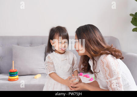 Bambina e la sua mamma bere latte seduti sul divano di casa. La maternità e la cura, sana alimentazione e corretto stile di vita, precoce sviluppo concetto, copia spac Foto Stock