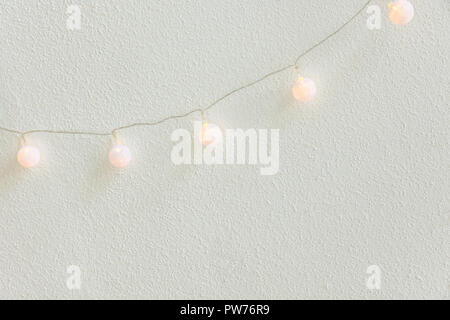 Natale Anno nuovo sfondo. Diagonale pastello pensili Golden palline di cotone Garland muro bianco sullo sfondo. Lo stile scandinavo. Luci scintillanti. Accogliente Foto Stock