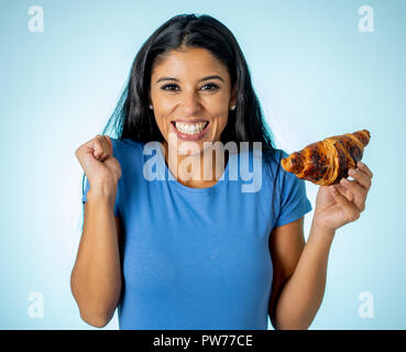 Giovane e bella carino e felice latino donna in abiti casual azienda big deliziosi croissant al cioccolato cercando con la tentazione di pensare se ignorando di Foto Stock