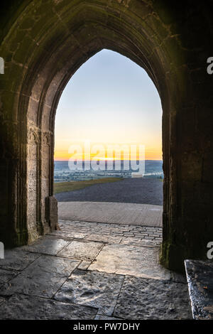 I primi raggi del tramonto illuminano le antiche pietre da lastrico di San Michele la torre sulla sommità di Glastonbury Tor in Somerset, Inghilterra. Foto Stock