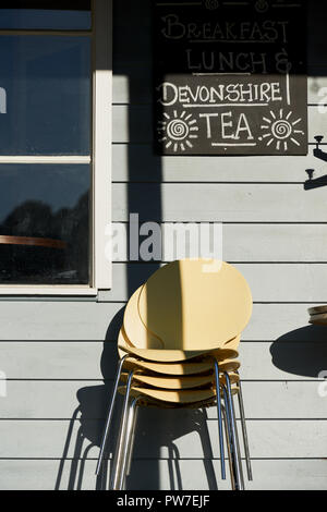 Giallo sedie impilate contro una parete con un segno al di fuori di un paese chiuso cafe. Foto Stock
