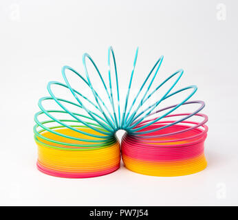 Slinky - un arcobaleno colorato giocattolo di plastica molla, isolato su sfondo chiaro. Foto Stock