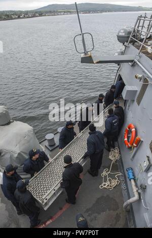 FASLANE in Scozia (sett. 23, 2017) velisti assegnati al Arleigh Burke-class guidato-missile destroyer USS Mitscher (DDG 57) riporre il brow come Mitscher si discosta di Sua Maestà la Base Navale di Clyde, Sett. 23, 2017. Mitscher, homeported in Norfolk, sta conducendo operazioni navali negli Stati Uniti Sesta flotta area di operazioni a sostegno degli Stati Uniti per gli interessi di sicurezza nazionali in Europa. Foto Stock