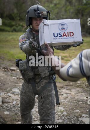 Stati Uniti Army Sgt. Delton Reynolds, un tecnico di volo, passa aiuti umanitari per un cittadino Domincan a Wotten Waven, Dominica, Ottobre 3, 2017. Il velivolo prelevato sacchi di riso e set da cucina DA PARTE DEGLI STATI UNITI Agenzia per lo Sviluppo Internazionale per la consegna alla comunità. Il servizio i membri della JTF-li stanno sostenendo la fornitura di aiuti umanitari per l'isola di Dominica dopo il passaggio dell uragano Maria. Su richiesta dei paesi partner e il Dipartimento di Stato e USAID, JTF-li ha distribuito degli aerei e i membri del servizio ad aree nella zona orientale del Mar dei Caraibi colpiti da hurrica Foto Stock