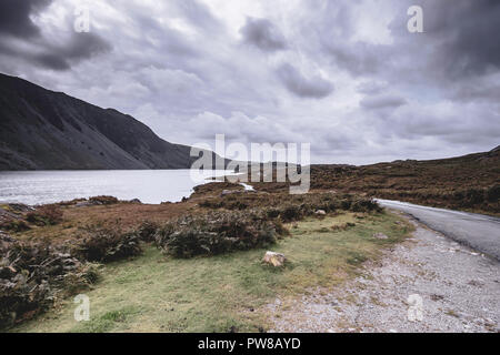 Strada rurale con poche pozzanghere dopo la pioggia trogolo scenic valle di montagna con vista sulle cime del Cumbria rurale nel Nord Ovest Inghilterra.drammatico cielo sopra il monte Foto Stock