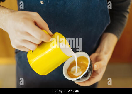 Chiusura del barista versando latte vaporizzato in una tazzina di caffè latte realizzazione tecnica. Foto Stock