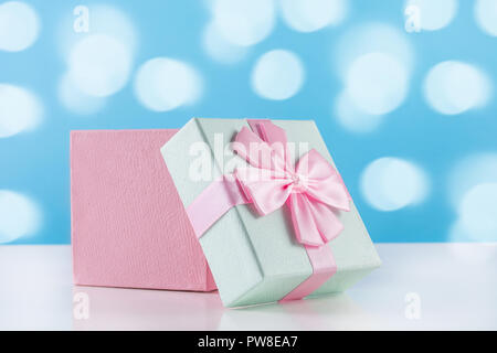 Rosa con delicatezza del regalo del bambino presente scatola con prua sulla scrivania bianca e blu sullo sfondo bokeh di fondo. Concetto di vacanza immagine. Close up, il fuoco selettivo Foto Stock