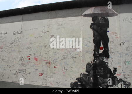 La sezione di East Side Gallery - muro di Berlino coperto di graffiti e stencil arte del ragazzo e ragazza baciare sotto un ombrello Foto Stock