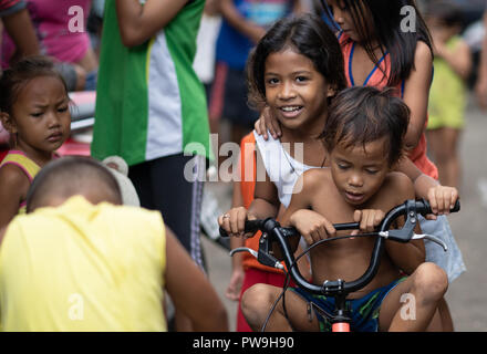 Una giovane ragazza filippina in sella ad una bicicletta con un altro bambino entro una delle baraccopoli di Cebu, Filippine Foto Stock