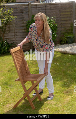 Donna apertura di un giardino pieghevole sedia in teak. Foto Stock