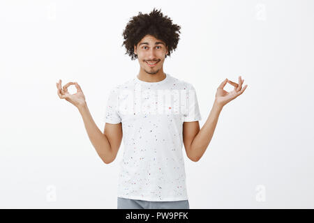 Calma e fare esercizi di yoga. Carefree affascinante meditazione lettino con acconciatura afro e baffi, tenendo le mani diffusione divagazioni zen con gesto sorridente con espressione rilassata, meditando Foto Stock