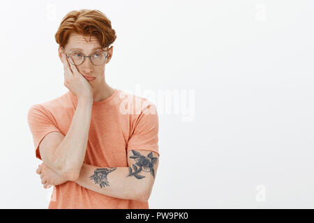 Elegante sleepy redhead guy cercando di non addormentarsi durante la classe, faccia pendente a portata di mano e di sguardo con stanco e espressione annoiata blackboard, in piedi indifferente e disattento, sognando il caffè Foto Stock