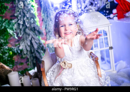 Incantevole piccola principessa in un abito bianco si siede su una slitta, getta neve fino e risate Foto Stock