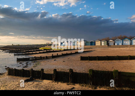 Cabine sulla spiaggia, pennelli e sulla spiaggia di ciottoli durante il pre-tramonto luce drammatica durante la primavera a Brightlingsea sulla costa di Essex, UK. Foto Stock