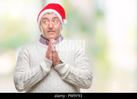 Bello il senior uomo con cappello a Natale su sfondo isolato a pregare con le mani insieme per chiedere perdono a sorridere fiducioso. Foto Stock