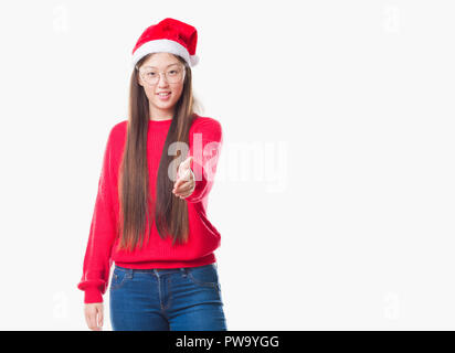 Giovane donna cinese su sfondo isolato con cappello a Natale sorridente cordiale offrendo stretta di mano come saluto e accogliente. Il successo dell'azienda. Foto Stock