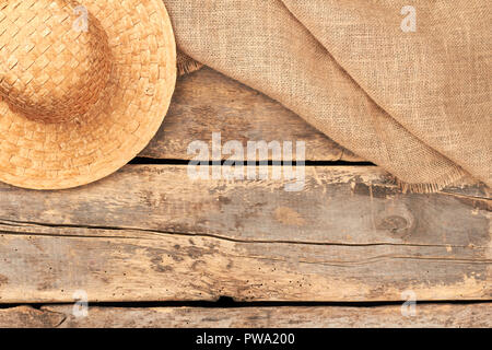 Tela hessian saccheggi e cappello di paglia. Piatto sfondo laici con cappello di paglia e tela di tessuto su rustico pavimento in legno. In stile vintage. Foto Stock