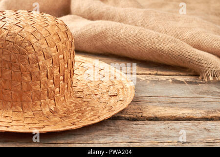 Cappello di paglia sul legno rustico sfondo. In vimini naturale hat e hessian panno in tessuto su tavole di legno. Foto Stock