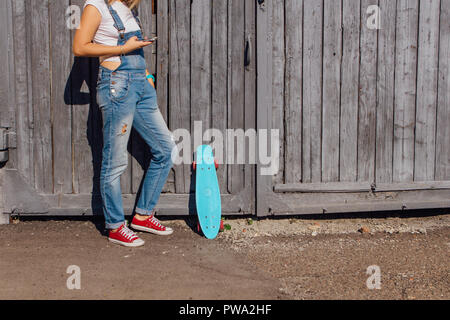 Chiudere i piedi di una ragazza in rosso sneakers e blue penny skateboard con ruote rosa in piedi accanto alla parete. Scena urbana, la vita della città. Sport e fitness Foto Stock