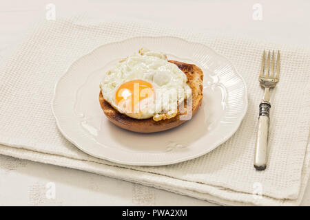 Uovo fritto sulla pianura bagel servita su bianco piastra ornamentali e sfondo bianco Foto Stock