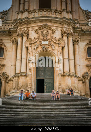 I turisti in appoggio sulle scale del Duomo di San Giorgio a Modica, splendido esempio di barocco siciliano art. La Sicilia Il sud dell'Italia. Foto Stock