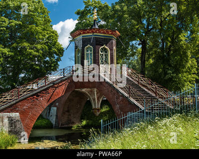 Pietra di mattoni rossi ponte con gazebo in stile cinese sulla parte superiore con grandi finestre traforata sopra l'acqua in estate in una giornata di sole in estate in Alexan Foto Stock