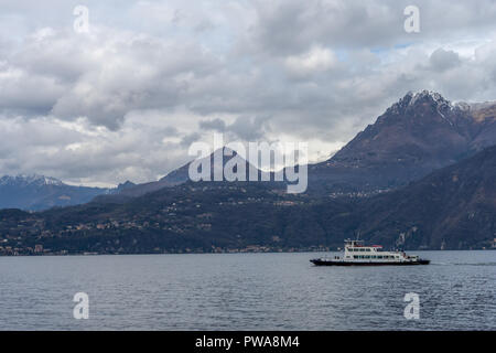 Varenna, Italia- 31 Marzo 2018: una barca sul Lago di Como il trasporto di autovetture per il villaggio di Varenna con una montagna in background Foto Stock