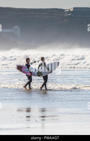 Surfers che trasportano le loro tavole da surf a piedi in mare a Fistral Beach in Newquay in Cornovaglia. Foto Stock