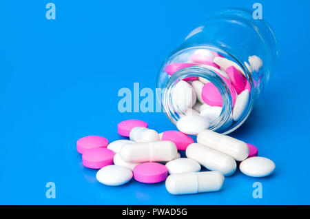 Vaso di vetro con sparsi in bianco e rosa pillole su uno sfondo blu. Foto Stock