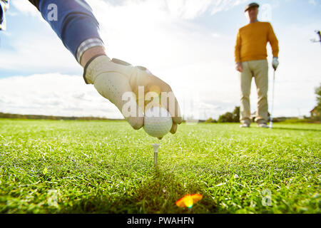 Uno dei giocatori di golf putting palla sul tee mentre l altro in piedi sullo sfondo Foto Stock