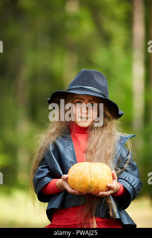 Bambina in giacca nera e hat holding mature zucca di Halloween mentre guardando a voi Foto Stock