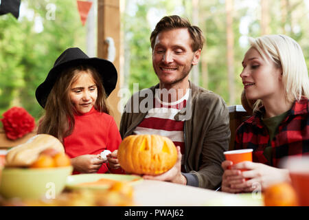 Giovane Azienda jack-o-lantern mentre seduti a tavola festiva tra la moglie e la figlia piccola Foto Stock