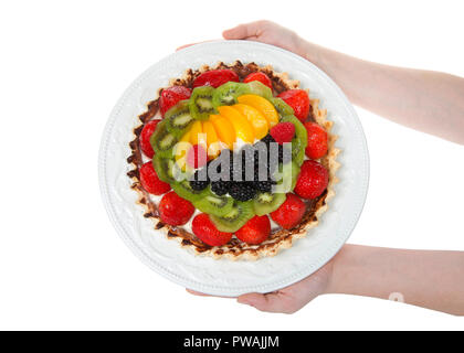 Crema fresca compilato tart su una piastra con frutta fresca, fragole, kiwi, pesche, mora e lampone detenute da giovani mani femminili. Isolato Foto Stock