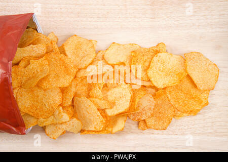 Barbecue al forno potato chips fuoriuscita del sacco di plastica sul legno chiaro tavolo. Lay piatto sopra la testa vista. Foto Stock