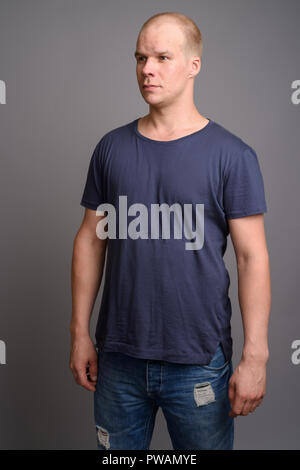 Uomo calvo indossando maglietta blu contro uno sfondo grigio Foto Stock