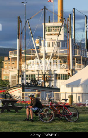 Whitehorse, Canada. SS. Klondike battello a vapore con ciclista seduta su una panchina di fronte in un giorno di estate. Foto Stock