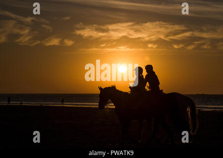 Silhouette di due donne a cavallo sulla spiaggia al tramonto Foto Stock