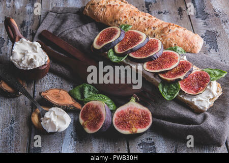 Bruschetta con crema di formaggio fichi e foglie di spinaci, su una superficie in legno, stile rustico Foto Stock