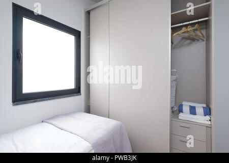 Piccola camera da letto con letto singolo e un armadio a aprire le porte scorrevoli e una grande finestra quadrata Foto Stock