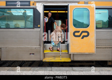 L'uomo aiuta una donna anziana utilizzando una stampella scendere dal treno Foto Stock