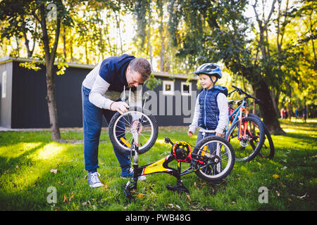 La festa del papà Caucasian papà e figlio di 5 anni nel cortile vicino alla casa sull'erba verde sul prato la riparazione di una bicicletta, di pompaggio di una bicicletta siamo Foto Stock