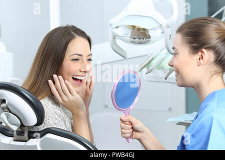 Felice dentista paziente controllo sbiancamento risultati guardando in uno specchio Foto Stock